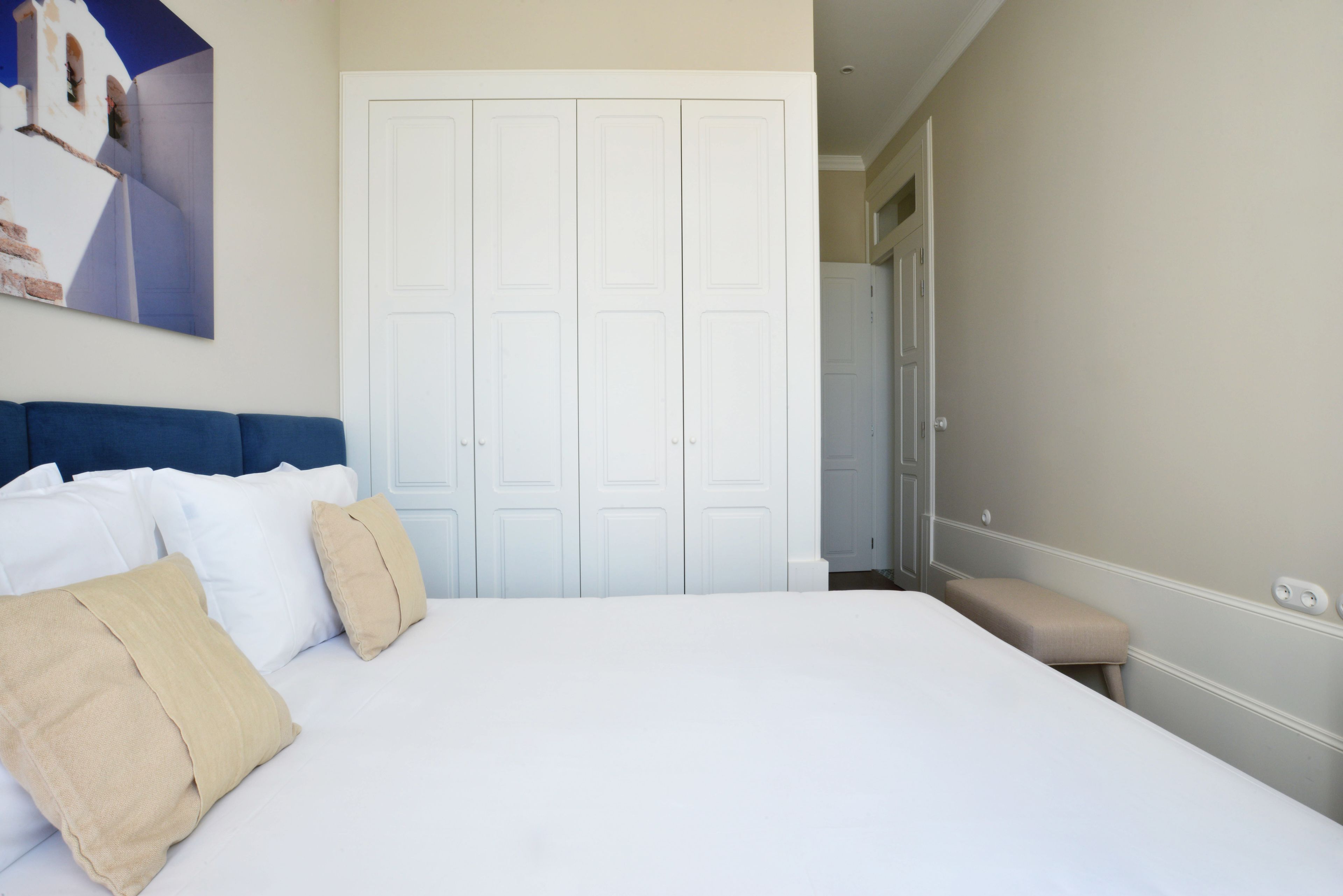A bedroom with a bed, white curtains, a bench, and a door.
