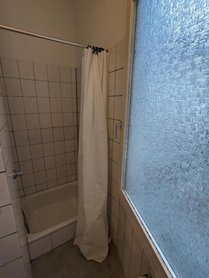 Et badeværelse med et badekar, en bruseforhæng og et vindue med sandblæst glas.