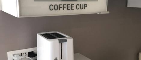 A kitchen with a toaster and a microwave on a countertop, a coffee cup symbol above a sign that reads "COFFEE CUP", and a cabinet with a hanging item.