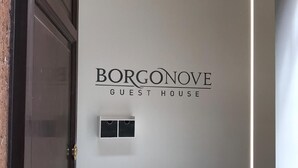 Eine Tür mit einem Schild, auf dem „BORGONOVE GUEST HOUSE“ steht, und einem kleinen Bedienfeld darunter.