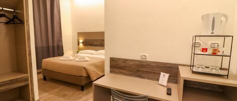A hotel room with a bed, a desk, a chair, a wardrobe, and a coffee machine.