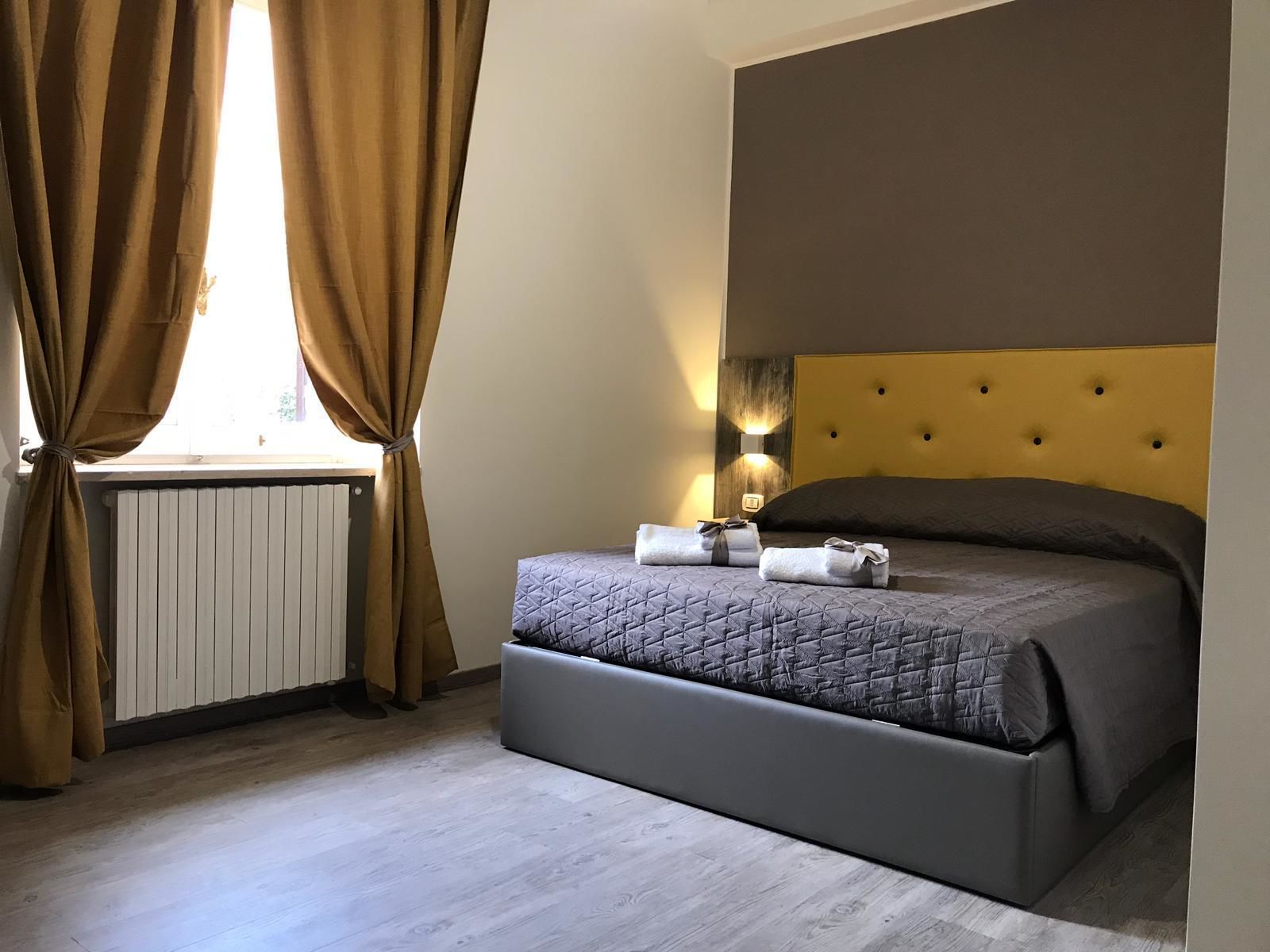 Une chambre à coucher avec un lit, des rideaux, un radiateur et une lampe fixée au mur.
