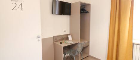 Une petite pièce comprenant un bureau, une chaise et un téléviseur fixé au mur.