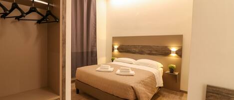 Un dormitorio ordenado con cama, mesitas de noche, armario y perchero con ropa.