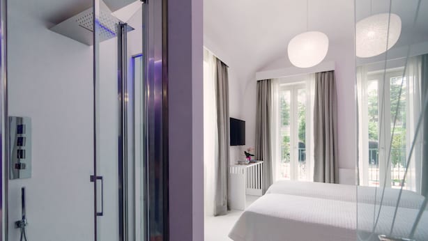 A modern hotel room with a large bed, a glass shower enclosure, a TV, and a balcony with curtains. - Ravello In (Ravello)