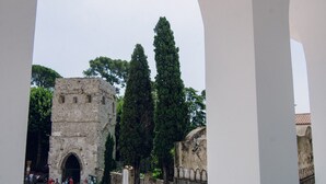 A historic stone building with an arched entrance, surrounded by tall trees and a white car parked nearby. - Ravello In (Ravello)