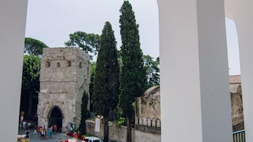 A historic stone building with an arched entrance, surrounded by tall trees and a white car parked nearby.