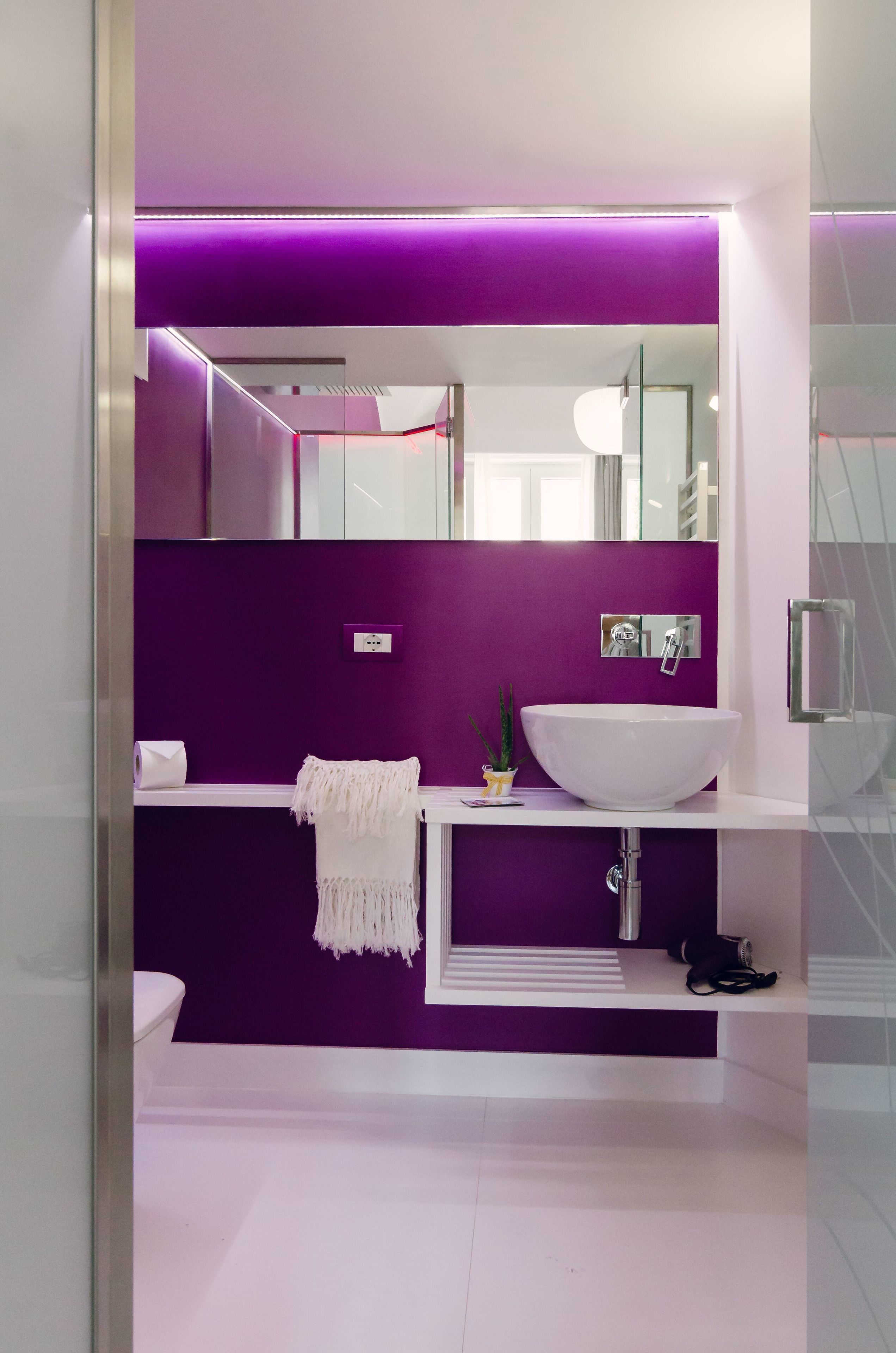Une salle de bain moderne avec un mur d’accent violet, un lavabo blanc et une douche à parois de verre.