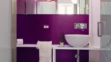 Une salle de bain moderne avec un mur d’accent violet, un lavabo blanc et une douche à parois de verre.
