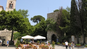 An outdoor cafe area with tables and chairs, surrounded by stone buildings and trees. - Ravello In (Ravello)