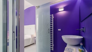 A modern bathroom with a white sink, purple walls, and a glass shower enclosure. - Ravello In (Ravello)