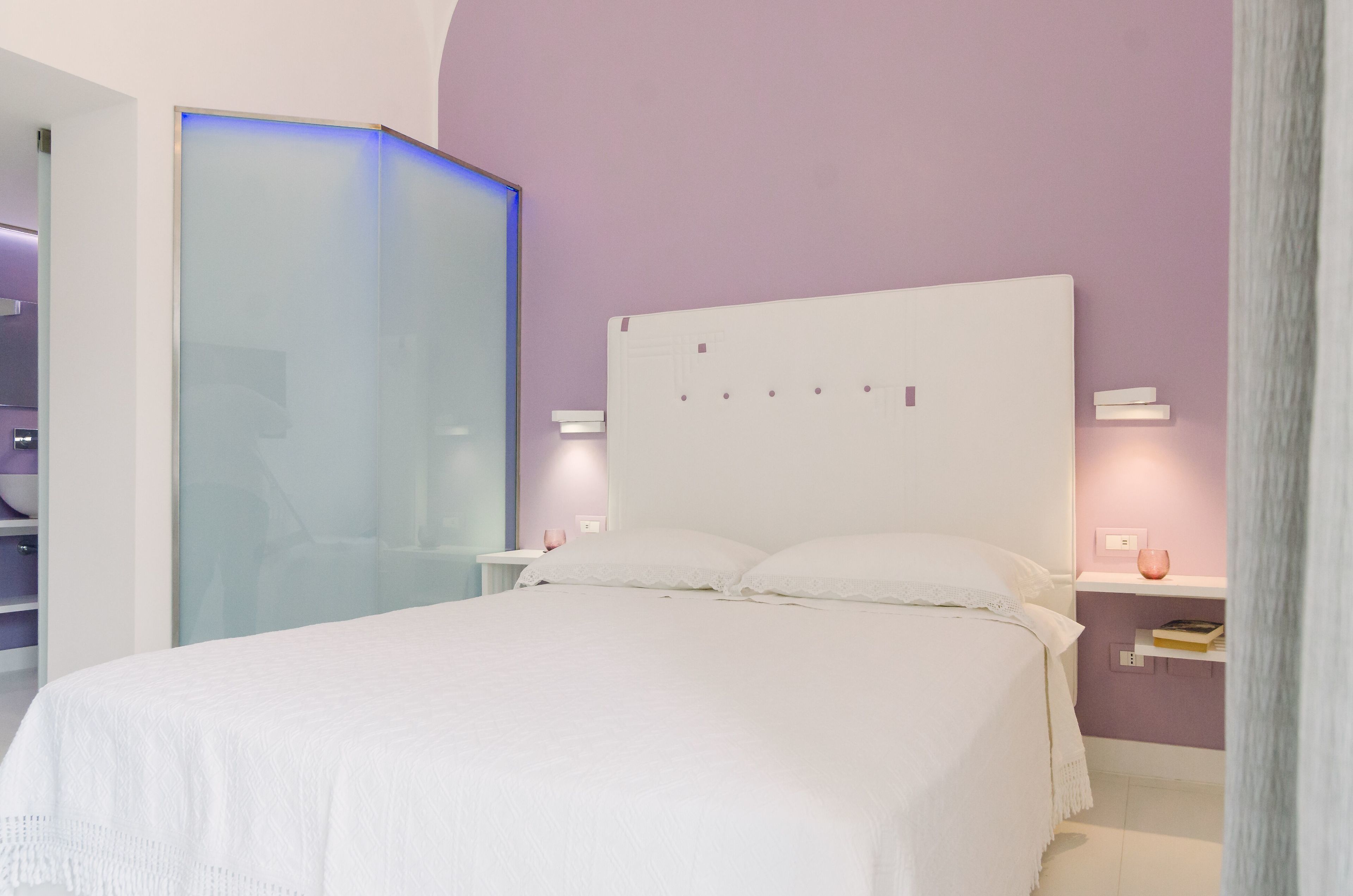 A modern bedroom with a large bed, a glass partition, and a purple accent wall.