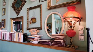 Une pièce avec une étagère en bois où sont rangés des livres et un téléphone à cadran, entourée de miroirs décoratifs et d’une lampe rouge.