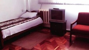 Um quarto pequeno com uma cama, uma televisão, uma cadeira e um radiador.