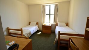 Quarto com duas camas de solteiro, uma escrivaninha com telefone e janela com cortinas.