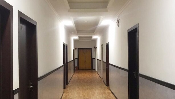 Um corredor comprido e estreito com piso de madeira e paredes brancas, com várias portas em ambos os lados.