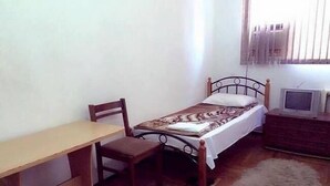 Um quarto pequeno com cama e escrivaninha de madeira, uma cadeira, uma televisão e um tapete.