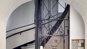 Una escalera conduce a un segundo piso, con una alfombra roja y una reja metálica con diseño decorativo.