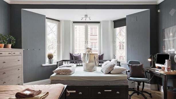 Un dormitorio con cama, escritorio, silla, cómoda y ventanas.