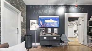 Una habitación moderna con una pared oscura, una consola Nintendo, una lámpara y una bicicleta en el umbral.