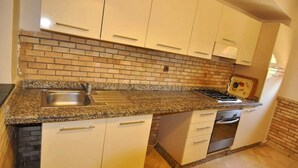 Una cocina con armarios blancos, encimera de granito, protector contra salpicaduras de ladrillo y estufa.