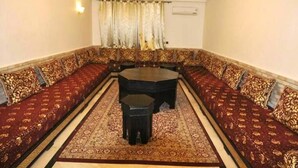 Una habitación con un sofá largo y decorado, orientado hacia una mesa central, un candelabro y cortinas estampadas.