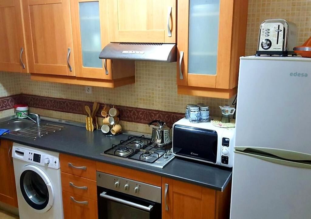 A kitchen with wooden cabinets, a washing machine, a stove, a microwave, and a toaster.
