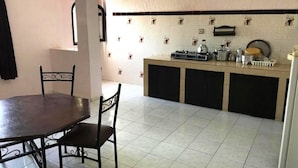 Una cocina con mesa y sillas, protector salpicado de azulejos y una encimera con diversos utensilios de cocina.