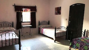 Un dormitorio con dos camas, una ventana con cortinas, una puerta y una mesita.