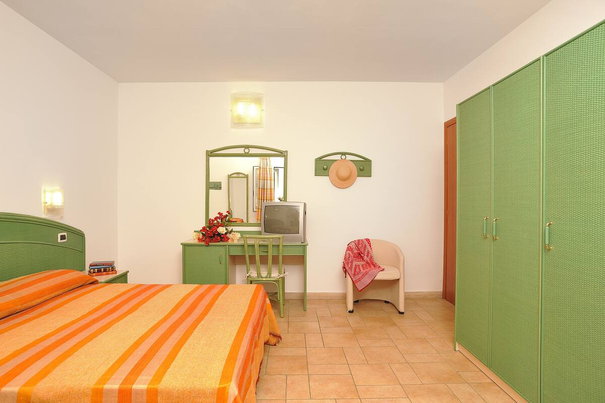 Une chambre à coucher comprenant un lit, un bureau avec une télévision, une chaise et une armoire.