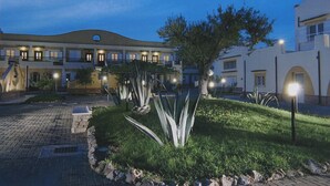A hotel courtyard with a paved walkway, a large tree, and a building with multiple balconies and lights. - Villaggio Turistico Le Meridiane (Montenero di Bisaccia)