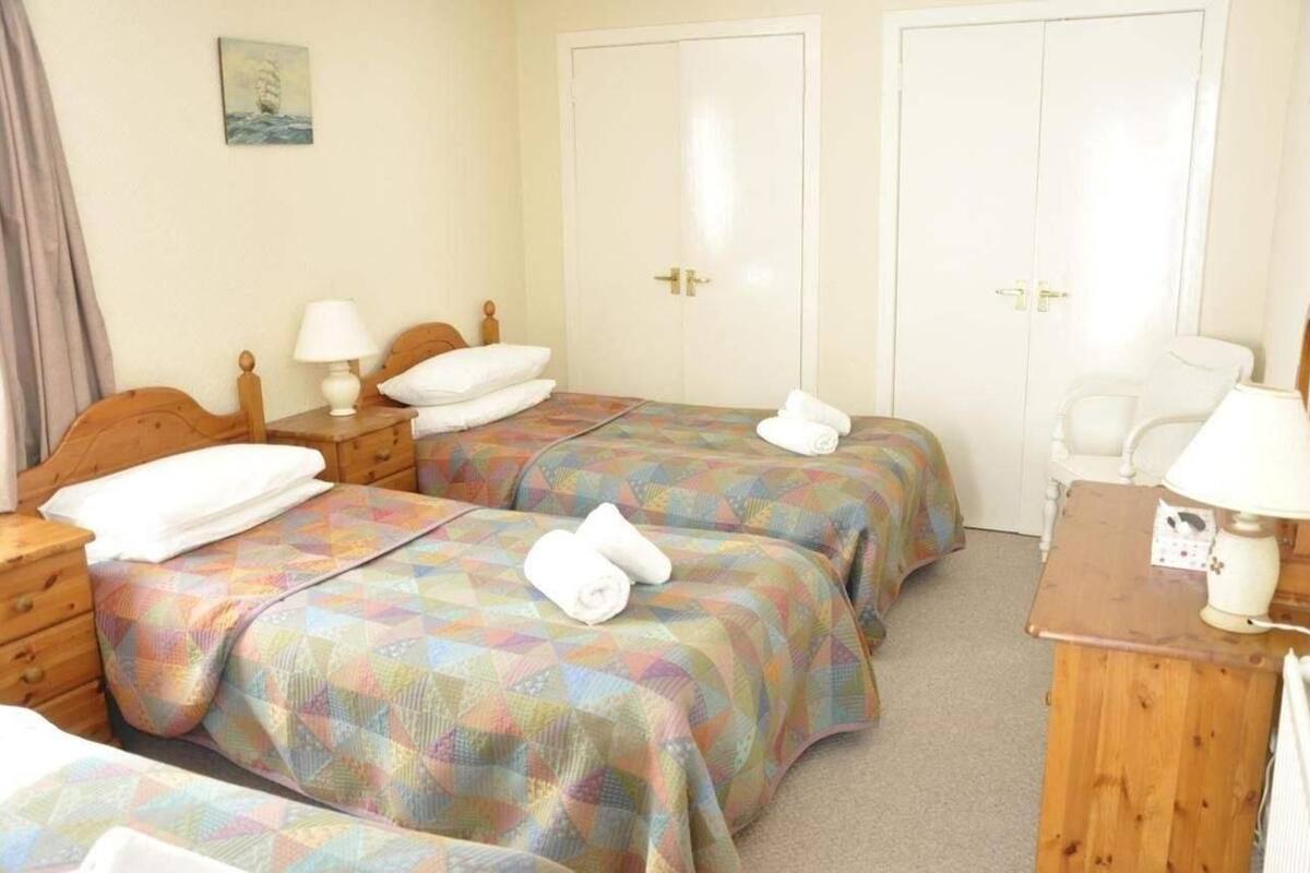 A hotel room with two beds, each with a colorful quilt, a wooden nightstand with a lamp, a chair, and a desk with a lamp.