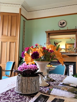 A dining area with a table set for two, featuring a vase of flowers, a rustic wooden planter, and a patterned tablecloth. - Buttonboss Lodge (Pitlochry)