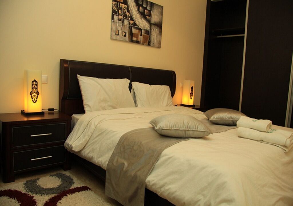 A neatly made bed with white and gray bedding, two bedside lamps, and a wall art piece above the bed.