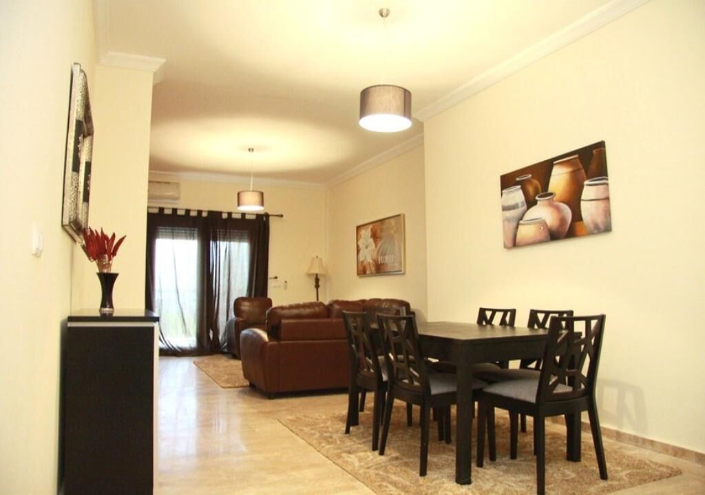 A dining area with a table and chairs, a sofa, and a painting on the wall.