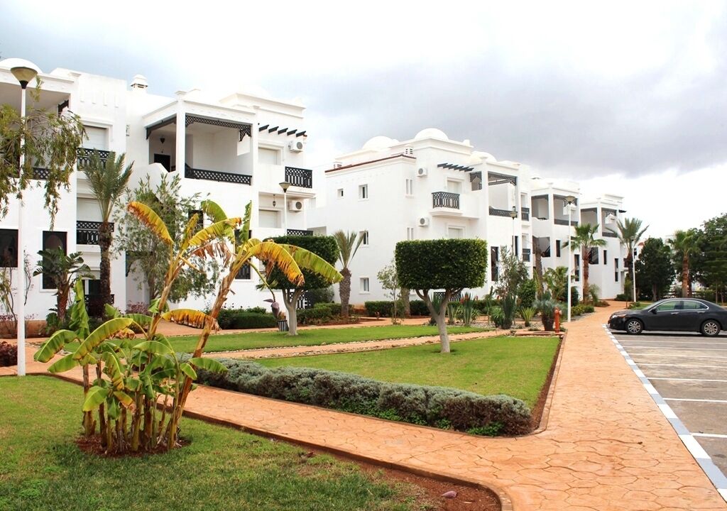 A residential building with multiple balconies, a paved driveway, and a parking area.