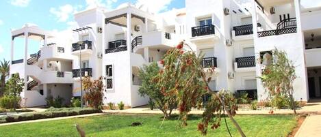 A white multi-story building with balconies, a well-maintained lawn, and a clear sky.