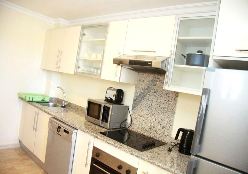 A compact kitchen with white cabinets, a granite countertop, a built-in oven, a microwave, a toaster, and a stainless steel refrigerator.