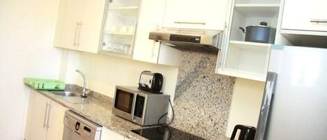 A compact kitchen with white cabinets, a granite countertop, a built-in oven, a microwave, a toaster, and a stainless steel refrigerator.