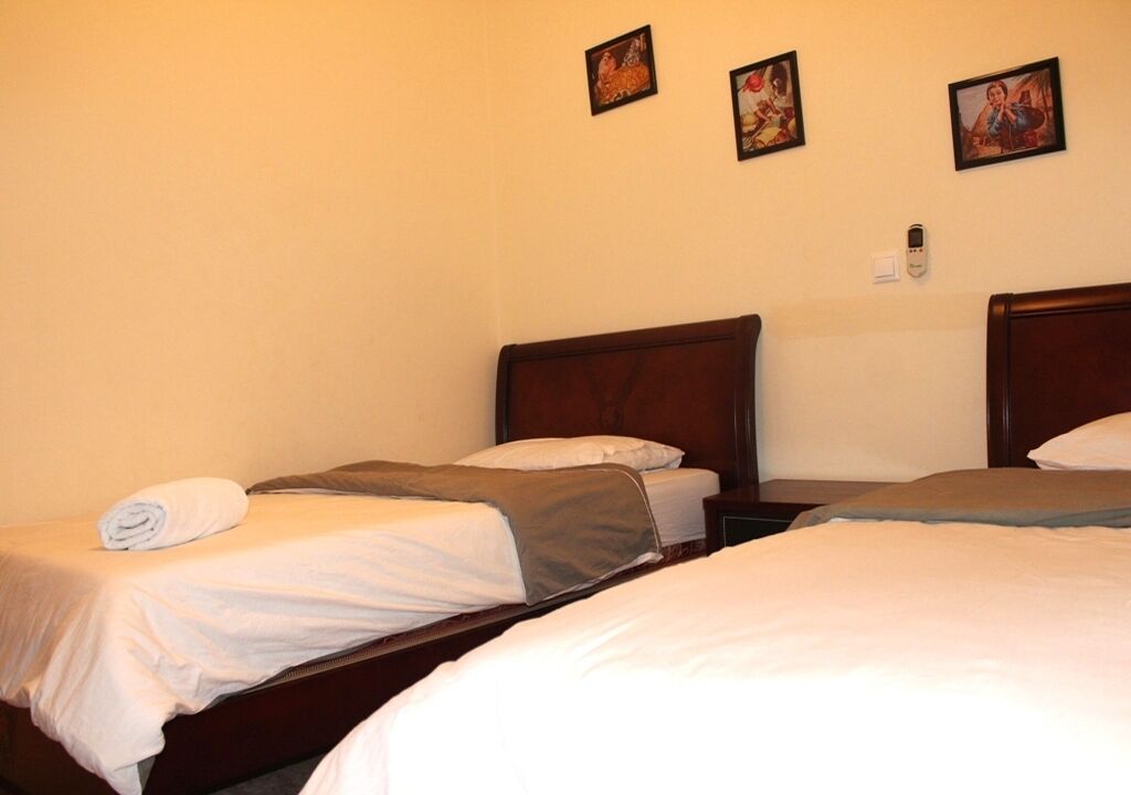 A hotel room with three single beds, each with a wooden headboard and white bedding. There are three framed pictures on the wall above the beds.