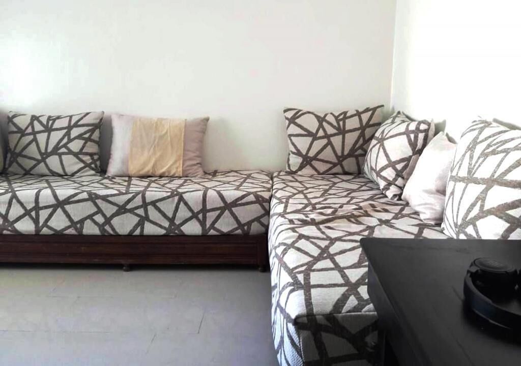 A modern living room with a sofa set featuring geometric patterned cushions, a dark wooden coffee table, and a small black object on the table.