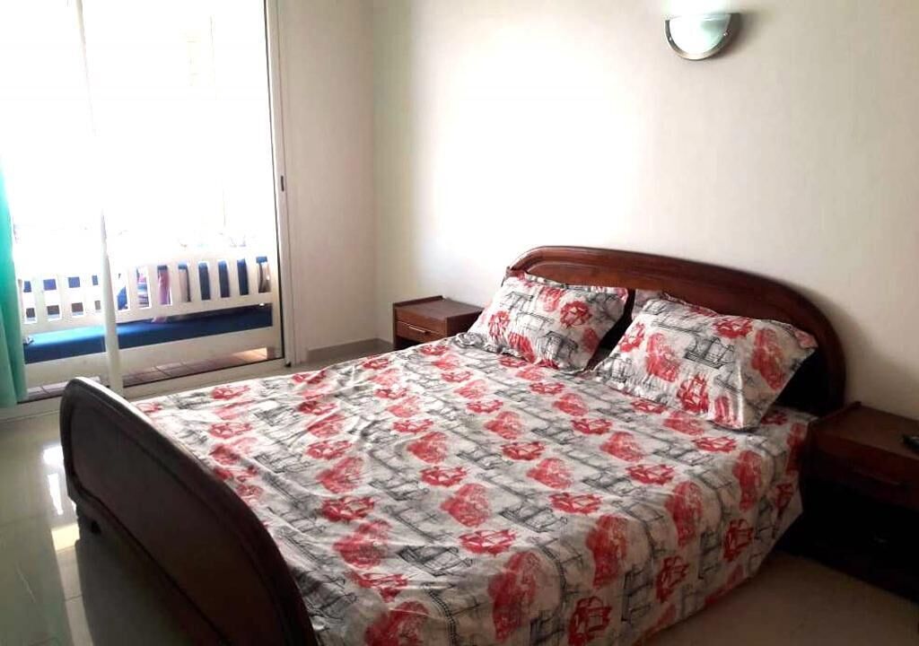 A bedroom with a bed, a nightstand, a wall-mounted lamp, and a view of a balcony.