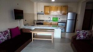A compact living space with a kitchenette, a TV mounted on the wall, and a sofa with floral cushions. - Atlantic Ocean Residence 3038 (Asilah)
