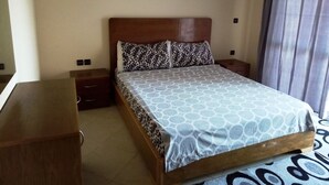 A hotel room with a bed, a wooden nightstand, a dresser, and a window with curtains. - Atlantic Ocean Residence 3038 (Asilah)