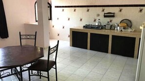 A kitchen with a dining table and chairs, a tiled backsplash, and a countertop with various kitchen items.