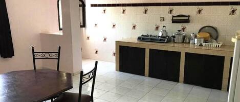 Una cocina con mesa y sillas, protector salpicado de azulejos y una encimera con diversos utensilios de cocina.