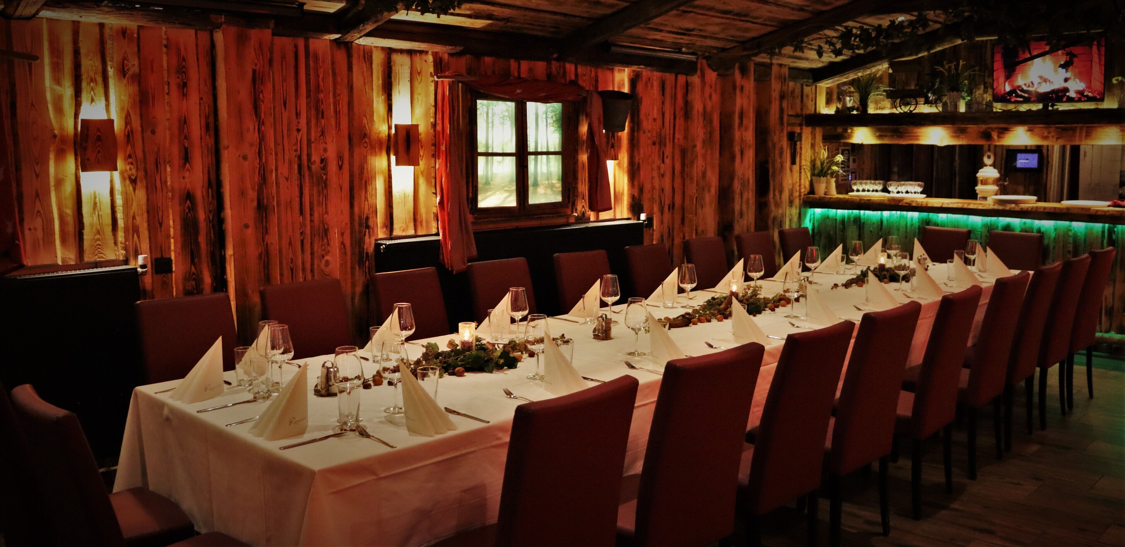 A long dining table set with white tablecloths, red chairs, and candles.