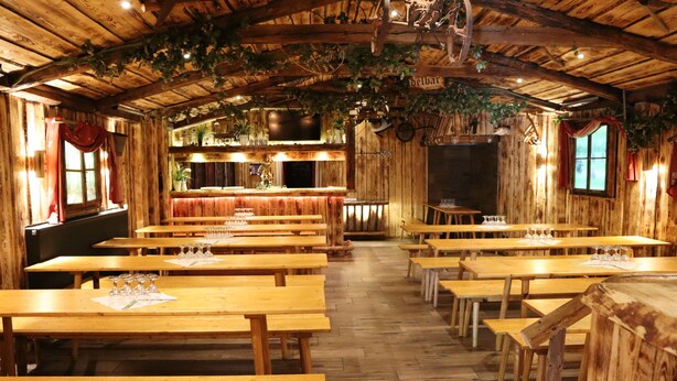 Un intérieur rustique en bois, avec de longues tables et des bancs, un coin bar et des plantes suspendues.