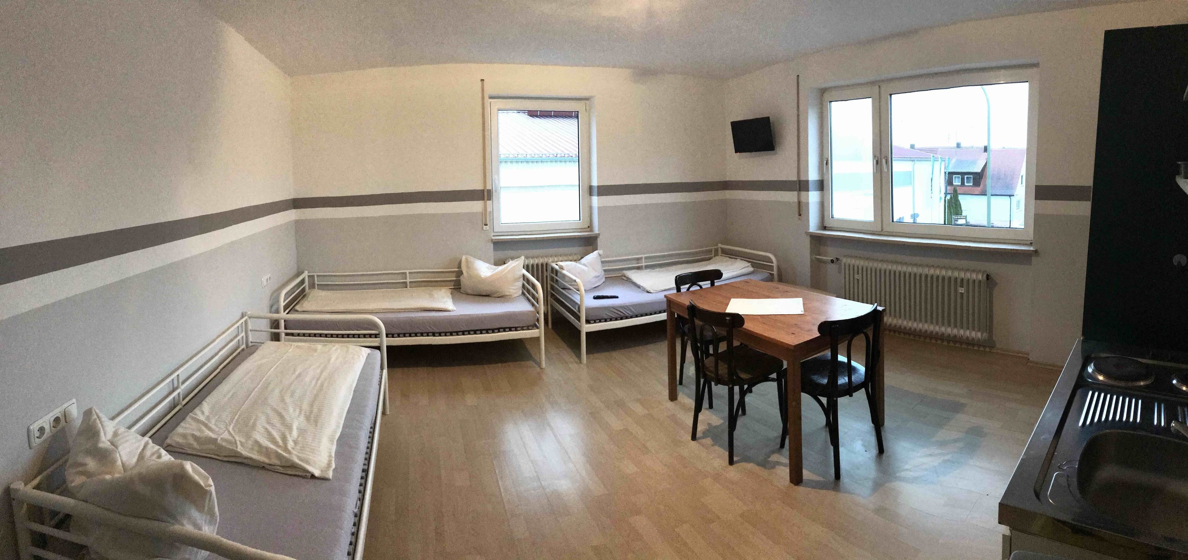 Un apartamento pequeño de una sola habitación con cama, una mesa con sillas, una ventana y un rincón de cocina.