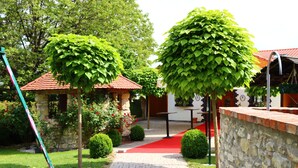 Un sentier de jardin mène à un bâtiment doté d’un toit rouge, entouré d’une végétation luxuriante et de murs en pierre.